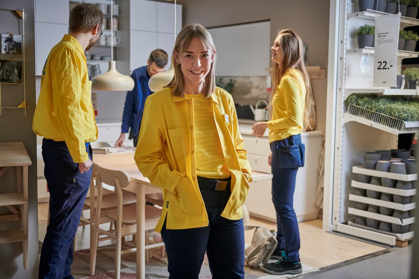Una empleada de IKEA sonríe en una sala de exposición mientras sus colegas trabajan detrás de ella.