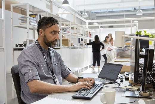 IKEA employee working at a computer desk in a modern, open-plan office.