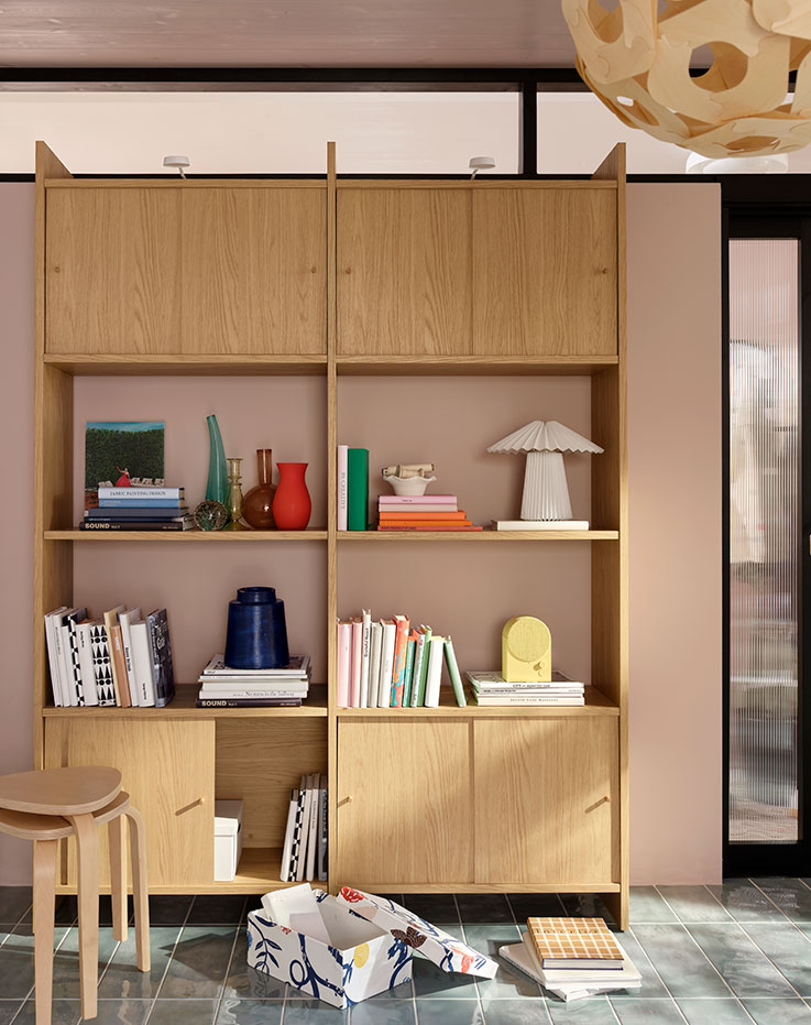 A bright living room with a light oak-effect LÅDMAKARE storage combination with sliding doors with books and decoration.