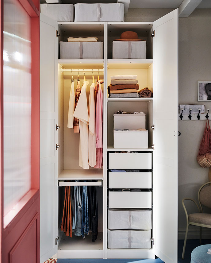A white PAX/TYSSEDAL wardrobe with the doors open showing organised clothes and two HEMMAFIXARE boxes on the top shelves.