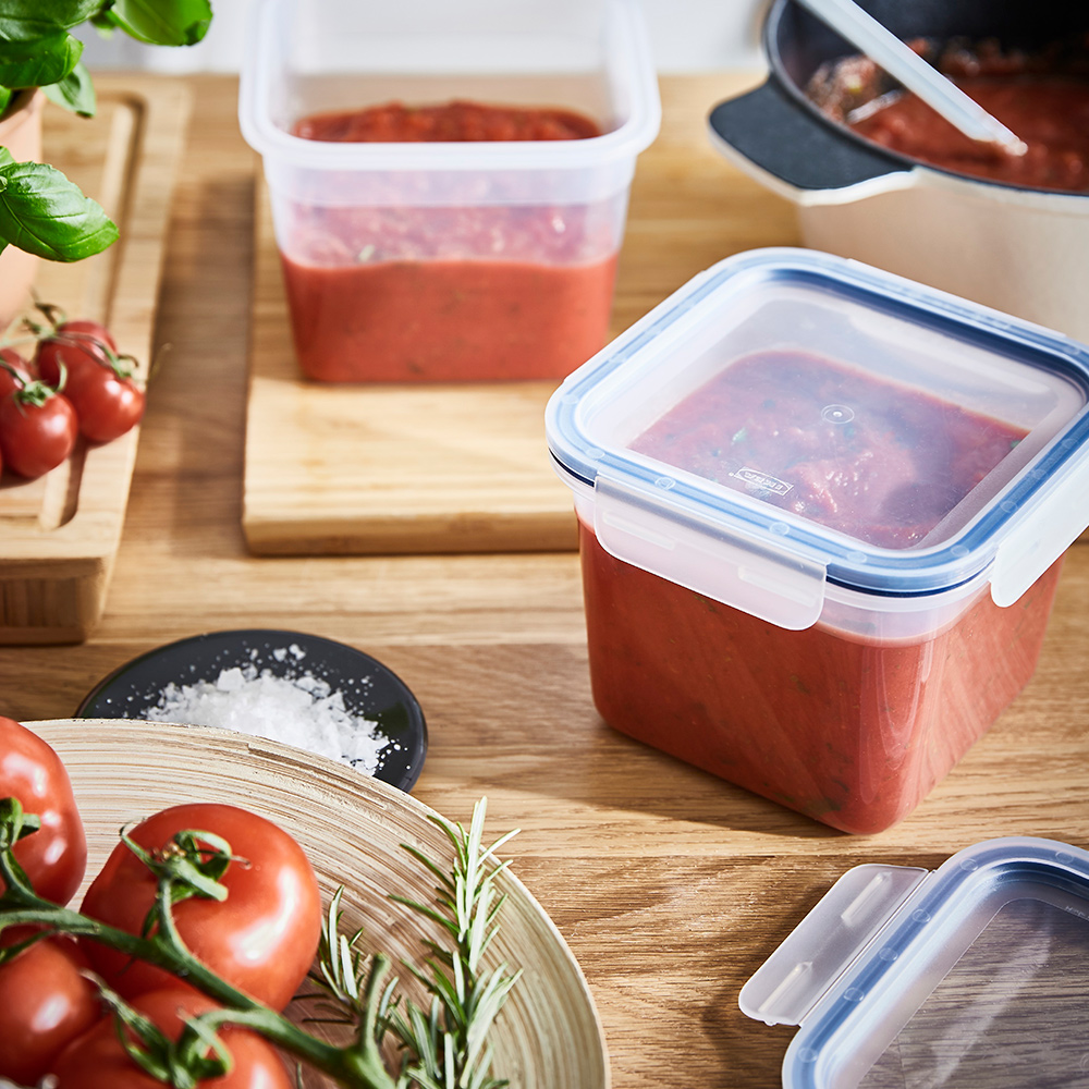 Two IKEA 365+ plastic food containers full of tomato sauce are on a wooden worktop in a kitchen.