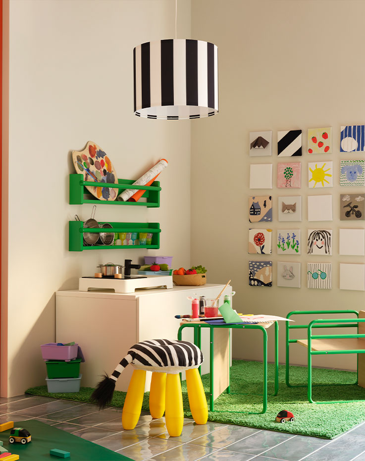 A corner with a green SMÅSKRAKE children’s chair-and table alongside a STENMUS play kitchen and colourful drawings.