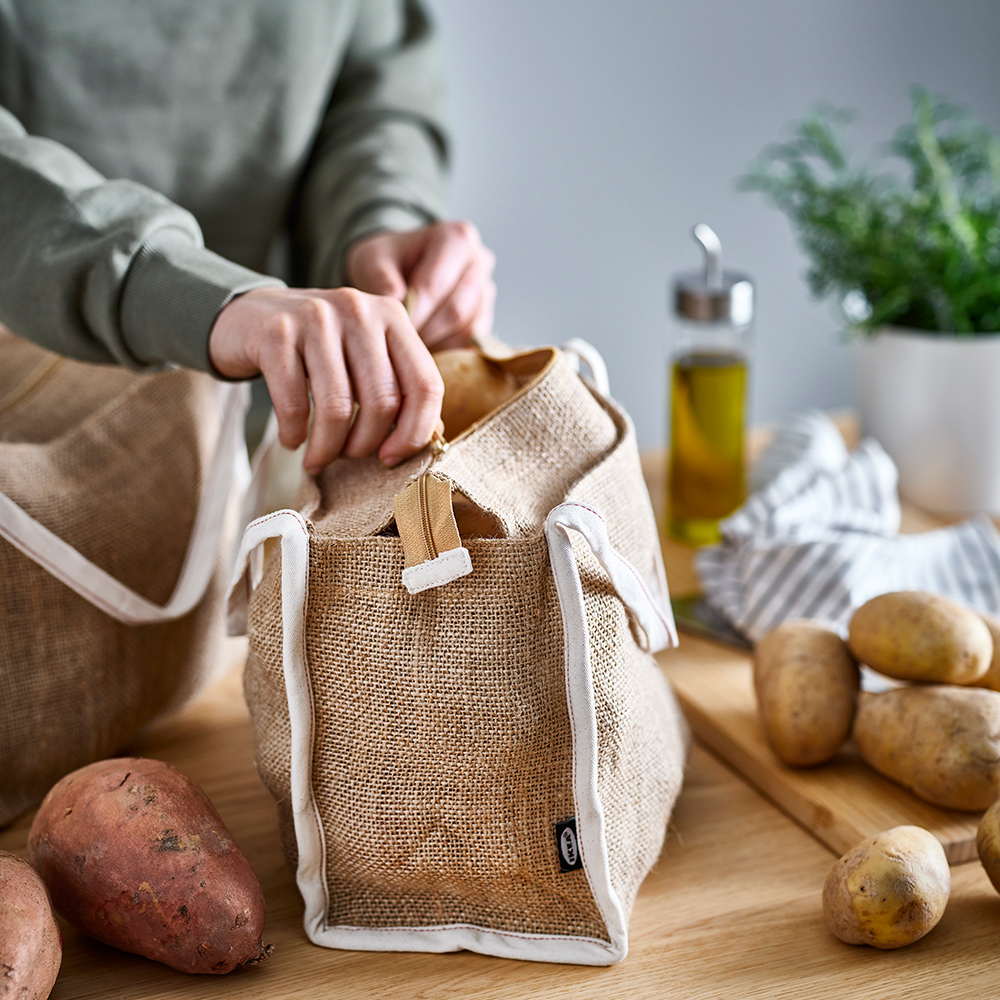 A person unzips a GULLRISMOTT food storage bag set on a kitchen worktop. Potatoes and sweet potatoes are on the worktop.