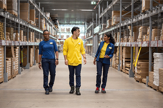 Three IKEA employees walk and smile down a large warehouse aisle. (62 caracteres)