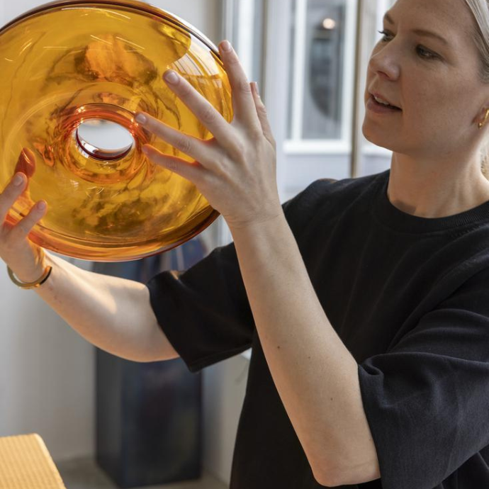 A woman holding and examining a circular, amber-colored glass object with a hole in the center.