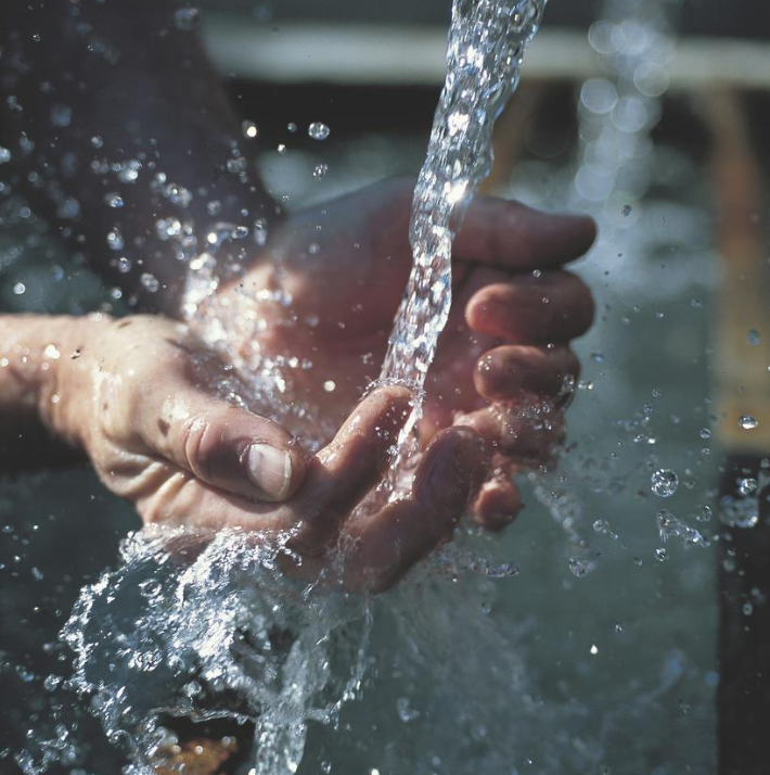 Close-up of water splashing into a person's cupped hands outdoors.