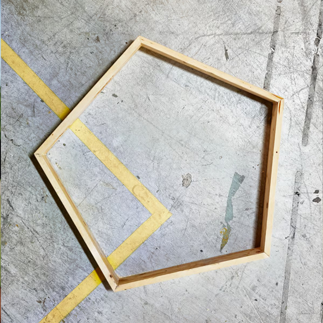 A pentagon-shaped wooden frame resting on an industrial concrete floor with painted yellow lines.