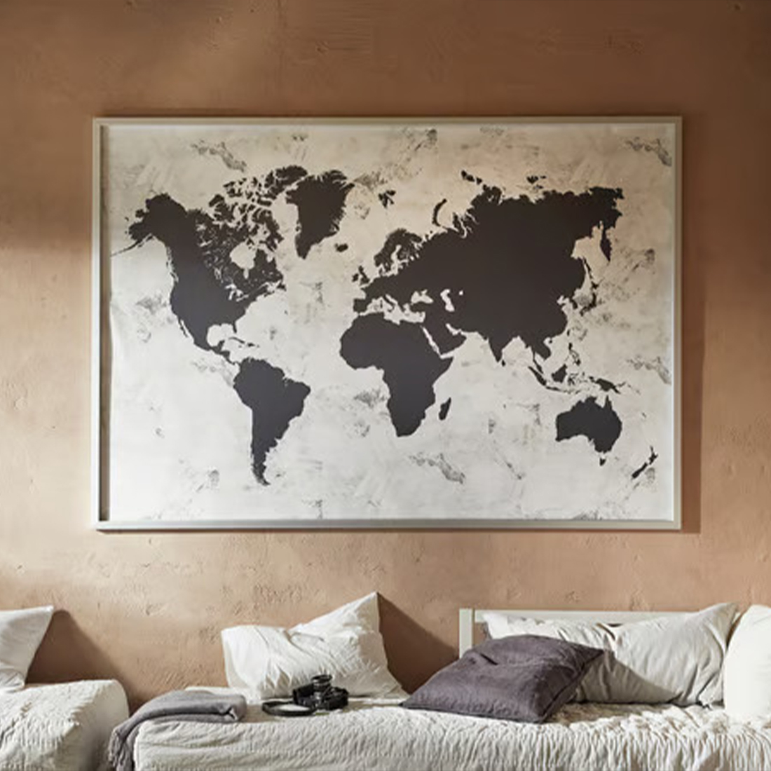 A minimalist black and white world map hanging above a bed with white and gray pillows, set in a room with earthy-toned walls.