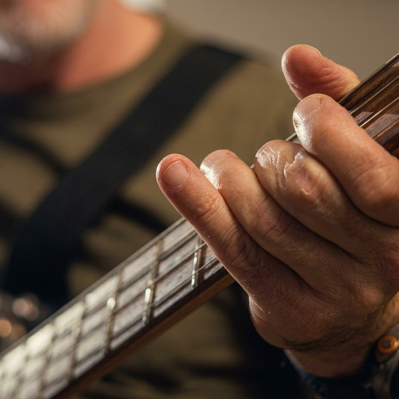 Close-up of a bass guitar neck being played by a musician on a stage with warm lighting.