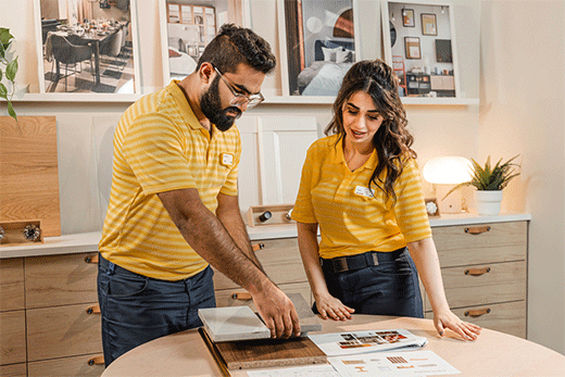 Two employees in yellow uniforms reviewing material samples on a showroom table.