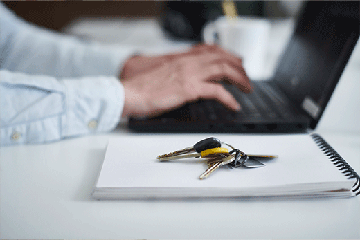 Un manojo de llaves sobre una libreta con una persona tecleando en una laptop.