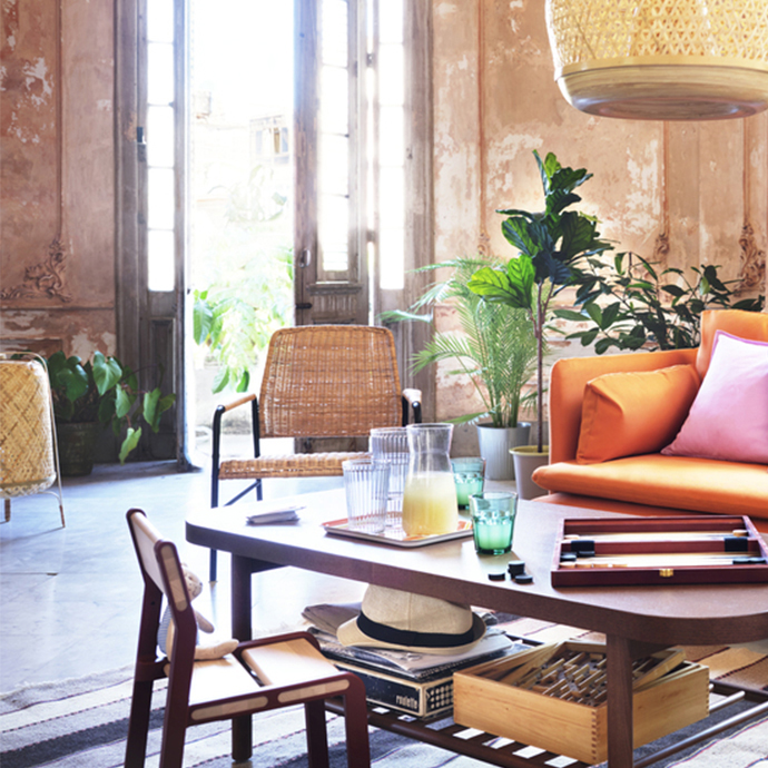 Sunlit rustic living room featuring an orange sofa, a wooden coffee table with a backgammon board, and a woven wicker lamp hanging above.